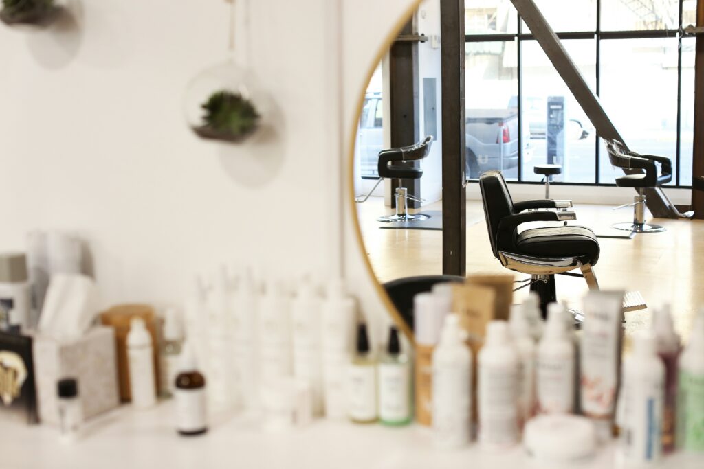 Wandregal mit Friseurprodukten, darüber ein Spiegel mit Spiegelung von Friseurstühlen