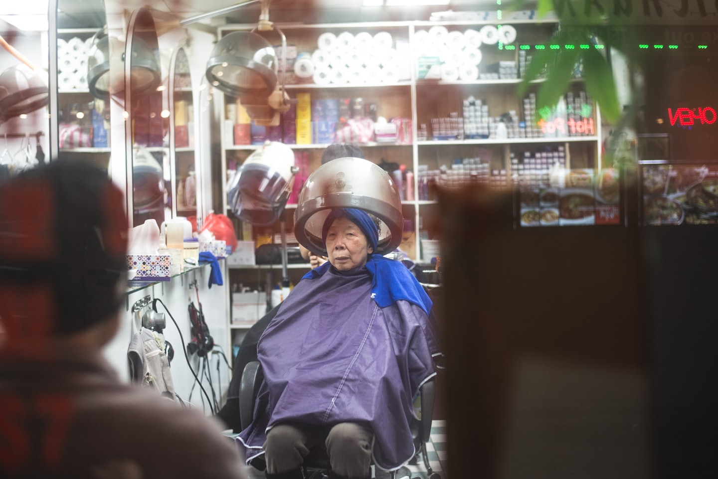 Ältere Dame beim Friseur unter Trockenhaube mit Blick zu einer weiteren Person